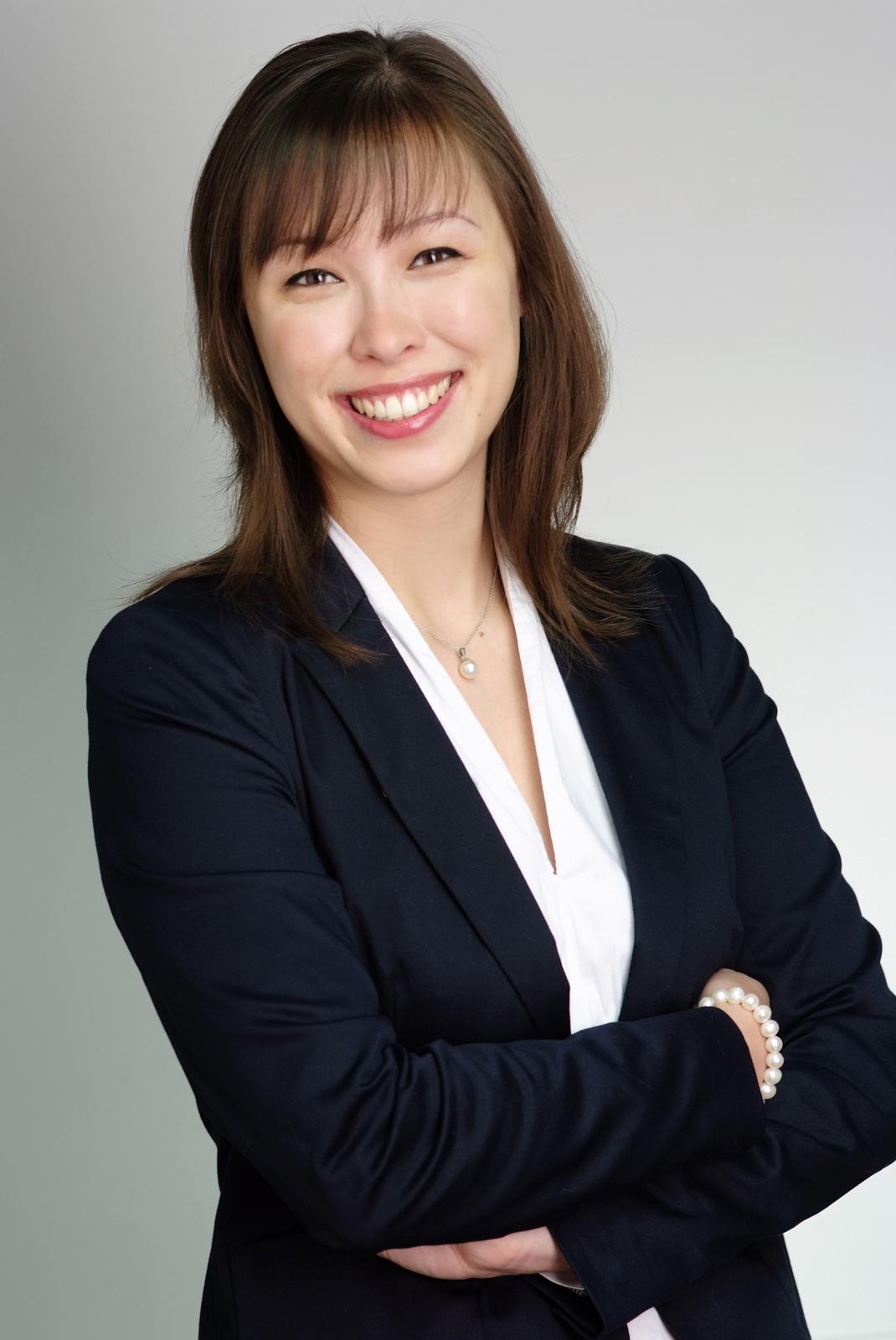 Stephanie has shoulder-length dark brown hair, dark brown eyes, and light brown skin. She is wearing a black blazer and a white shirt, has her arms crossed, and is smiling confidently at the camera.